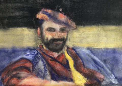 A bearded man in a colorful hat and scarf seated outdoors