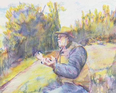 A seated man in a brimmed hat with his hands raised beside a sunlit woodland path