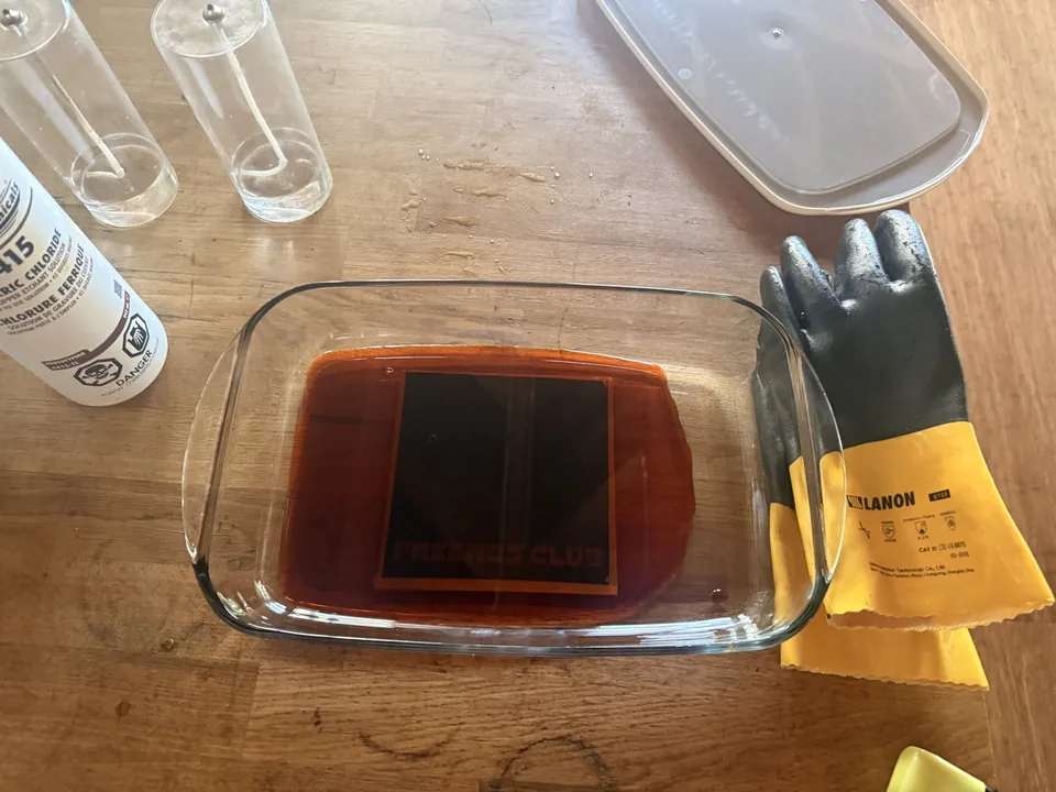 The brass plate etching in an orange bath of ferric chloride