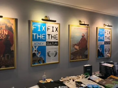 The Coined in Watercolor poster displayed among Bitcoin Film Festival posters above a table at Kinoteka.