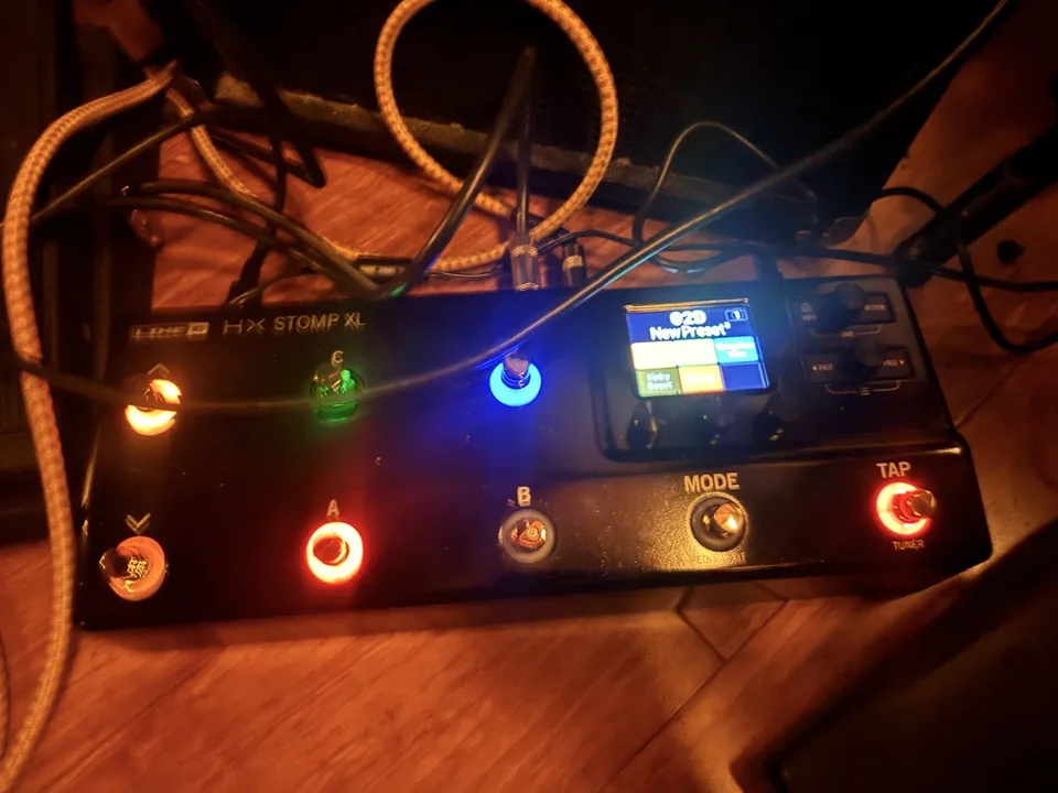 The Line 6 HX Stomp XL lit up on the floor, footswitches glowing red, green and blue, with the screen showing a new preset