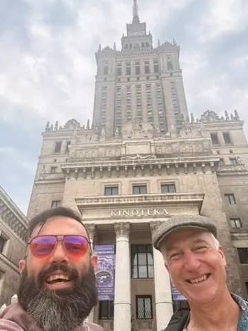 Two festival visitors smiling outside the Kinoteka entrance beneath the Palace of Culture and Science.