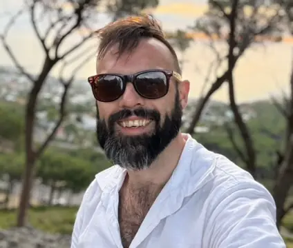TJ Murphy smiling outdoors in sunglasses and a white shirt