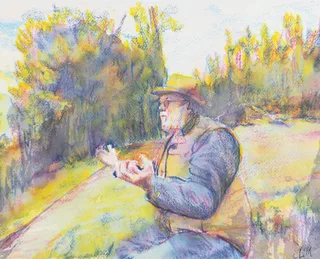 A seated man in a brimmed hat with his hands raised beside a sunlit woodland path